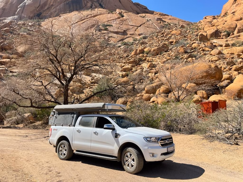 AHA Transformer on a white Ford Ranger An AHA Transformer mounted on a white Ford Ranger double cab, parked on sand among granite boulders and thorn trees in an arid landscape.