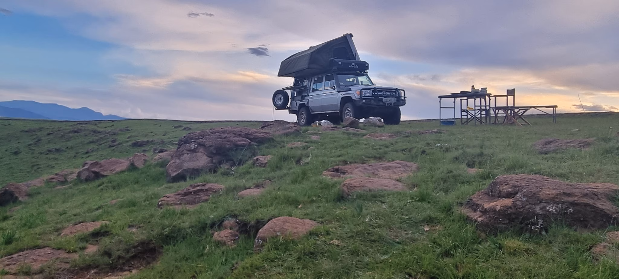 An AHA Transformer open on a Land Cruiser on a grass ridge, camp set up at dusk.