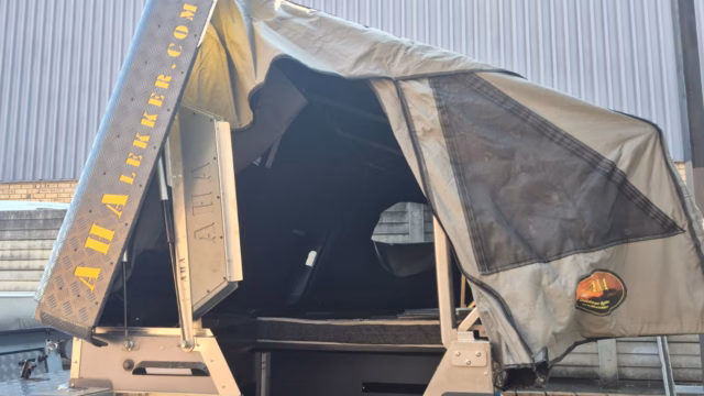 The roof of a pre-owned 2024 AHA Transformer fully opened. The lid lifted to the left (upright), and the right side flipped open (horizontally) to the right. Seen from behind, with the bed visible inside.